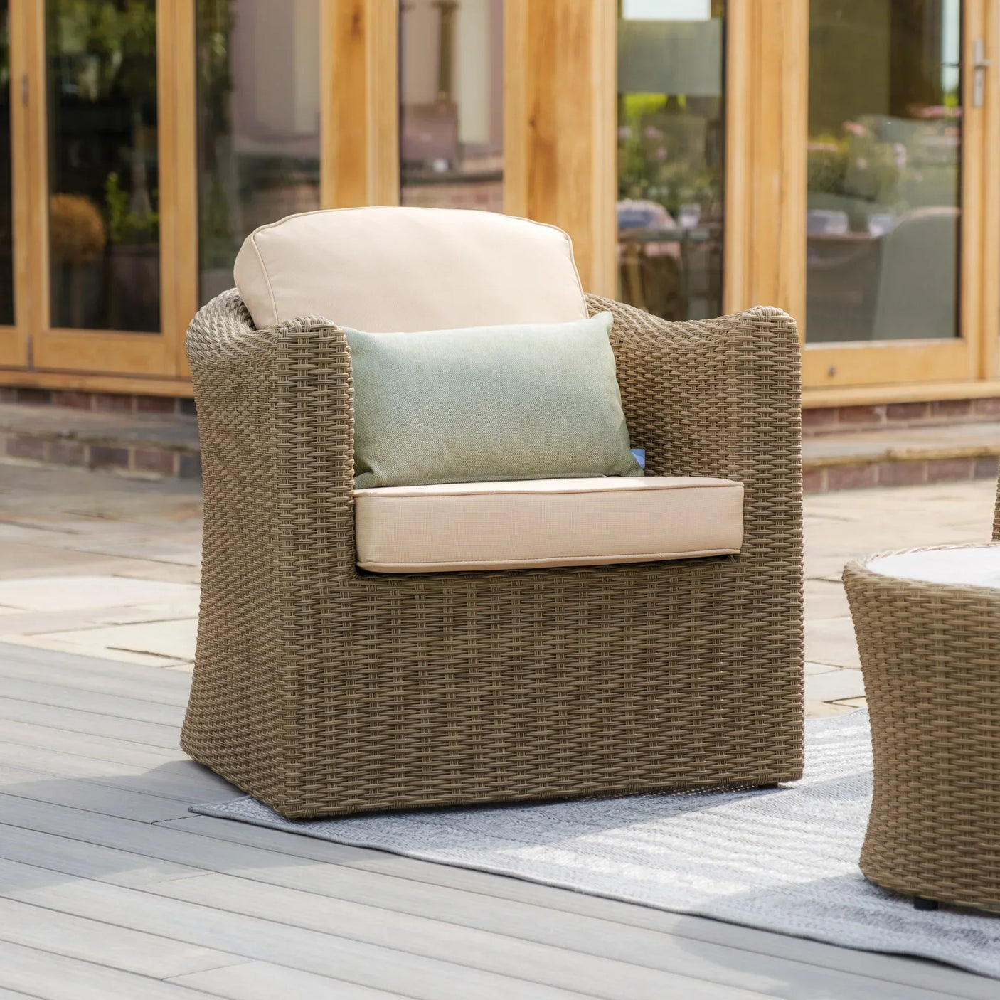 Rattan outdoor armchair with beige cushions and green accent pillow on patio decking
