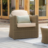 Rattan outdoor armchair with beige cushions and green accent pillow on patio decking