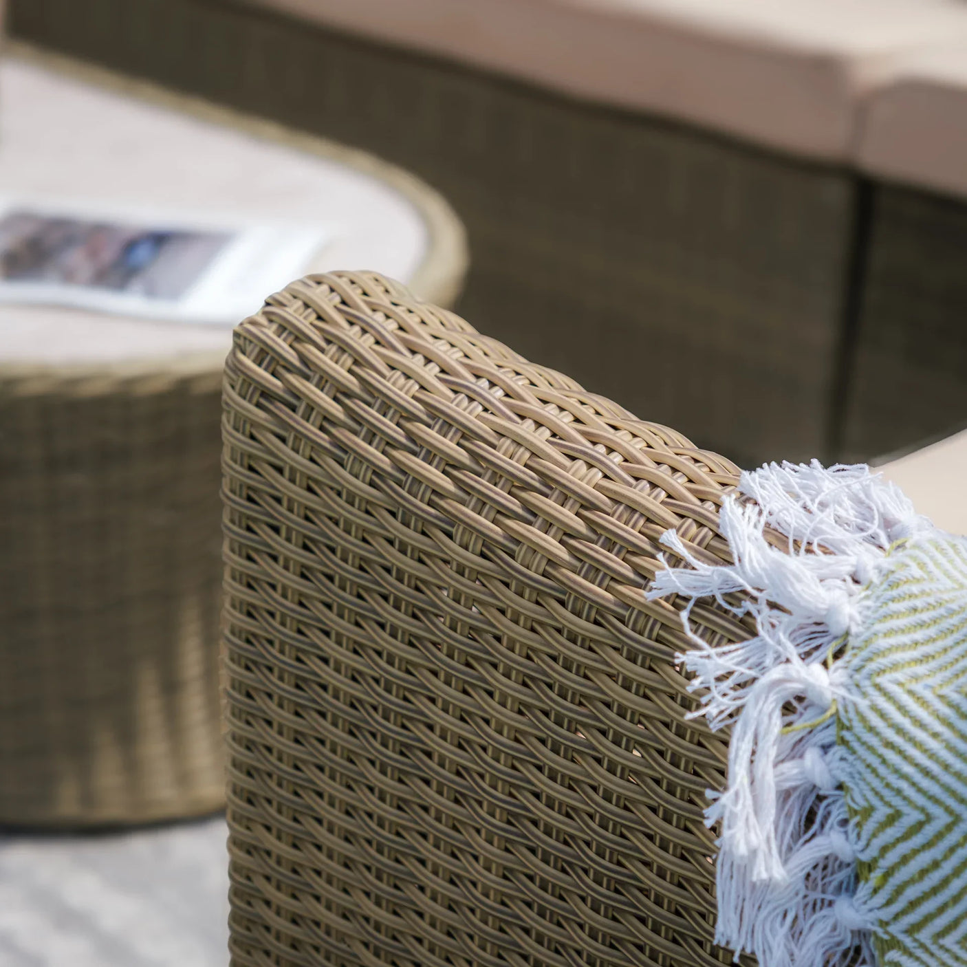 Close-up of rattan outdoor sofa arm with beige cushion and decorative throw
