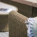 Close-up of rattan outdoor sofa arm with beige cushion and decorative throw