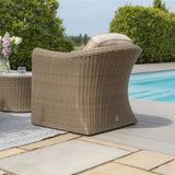 Rattan garden armchair with cushion by poolside on patio with greenery in background