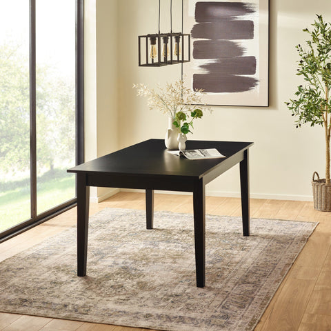 Black rectangular dining table with tapered legs, on patterned beige rug near large window and light wall art