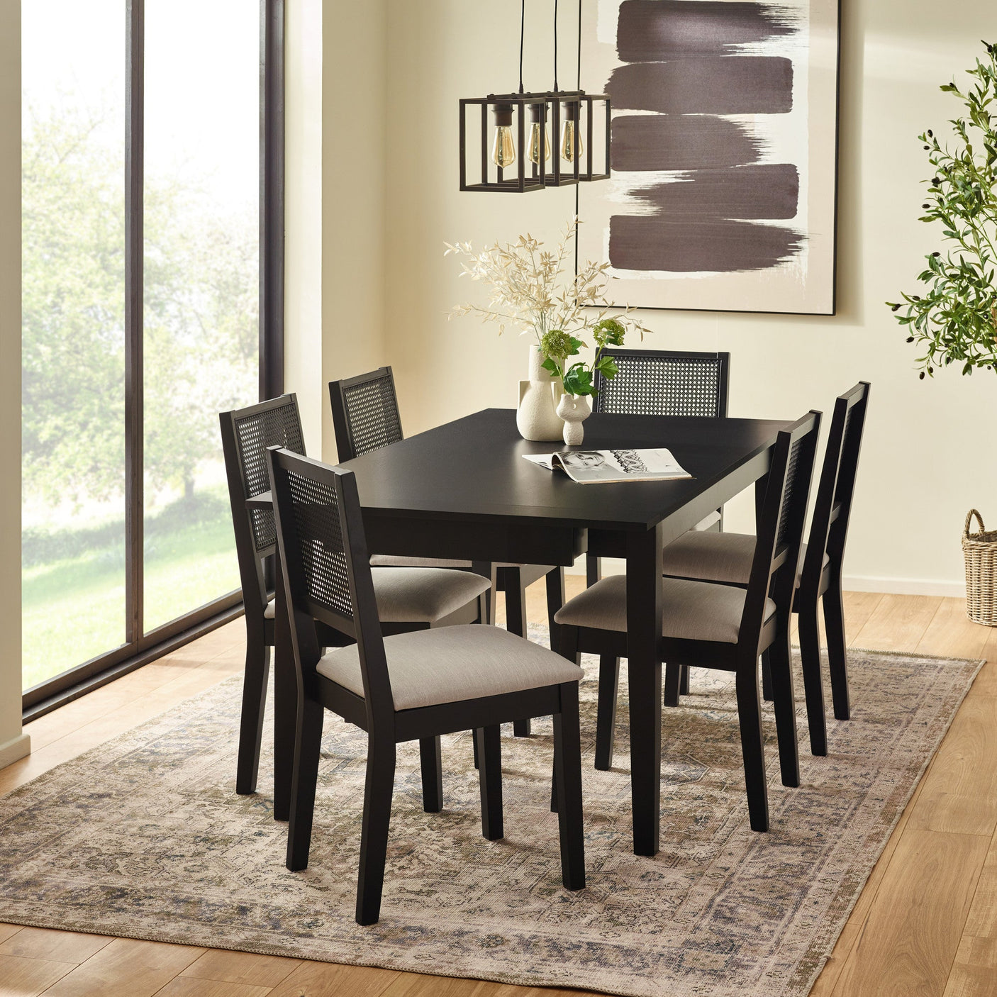 Black dining table with six chairs in bright room on patterned rug near window with pendant lights and wall art