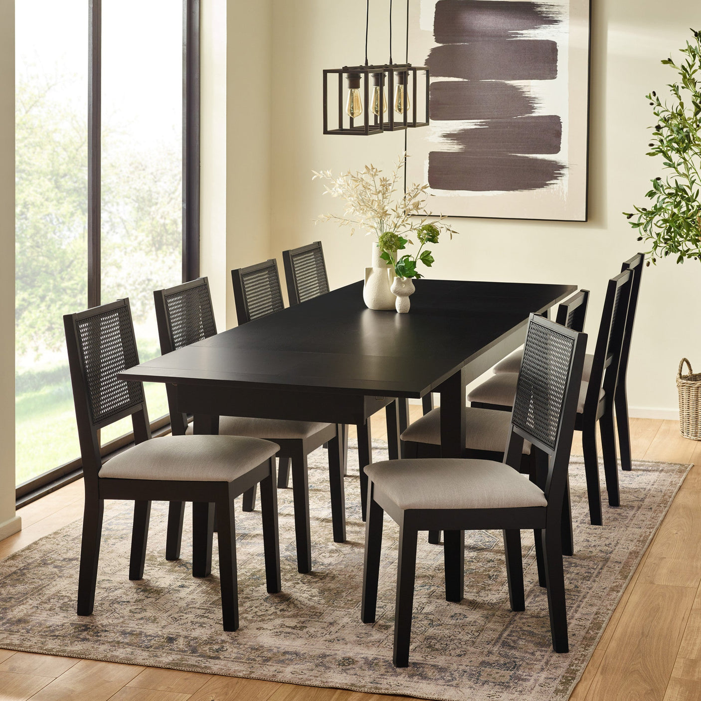 Black extending dining table with six black chairs and beige cushions, dining room setting with decor on table