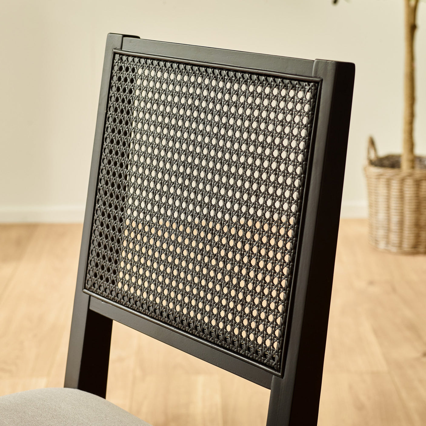 Close-up of black woven cane backrest on dining chair with light wood flooring background