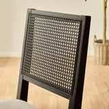 Close-up of black woven cane backrest on dining chair with light wood flooring background