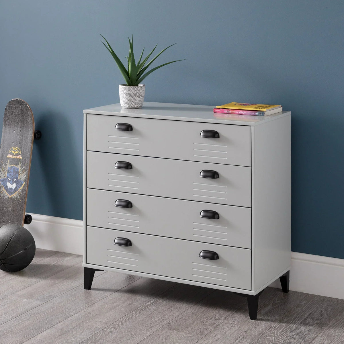 Grey 4 drawer chest with black handles, plant, and books in modern bedroom corner