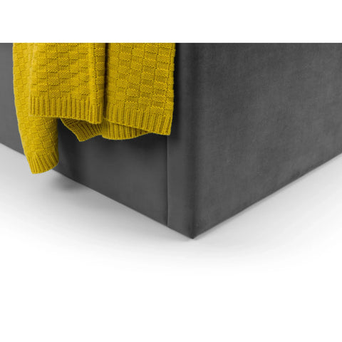 Close up of grey velvet storage ottoman with folded yellow knitted blanket on top