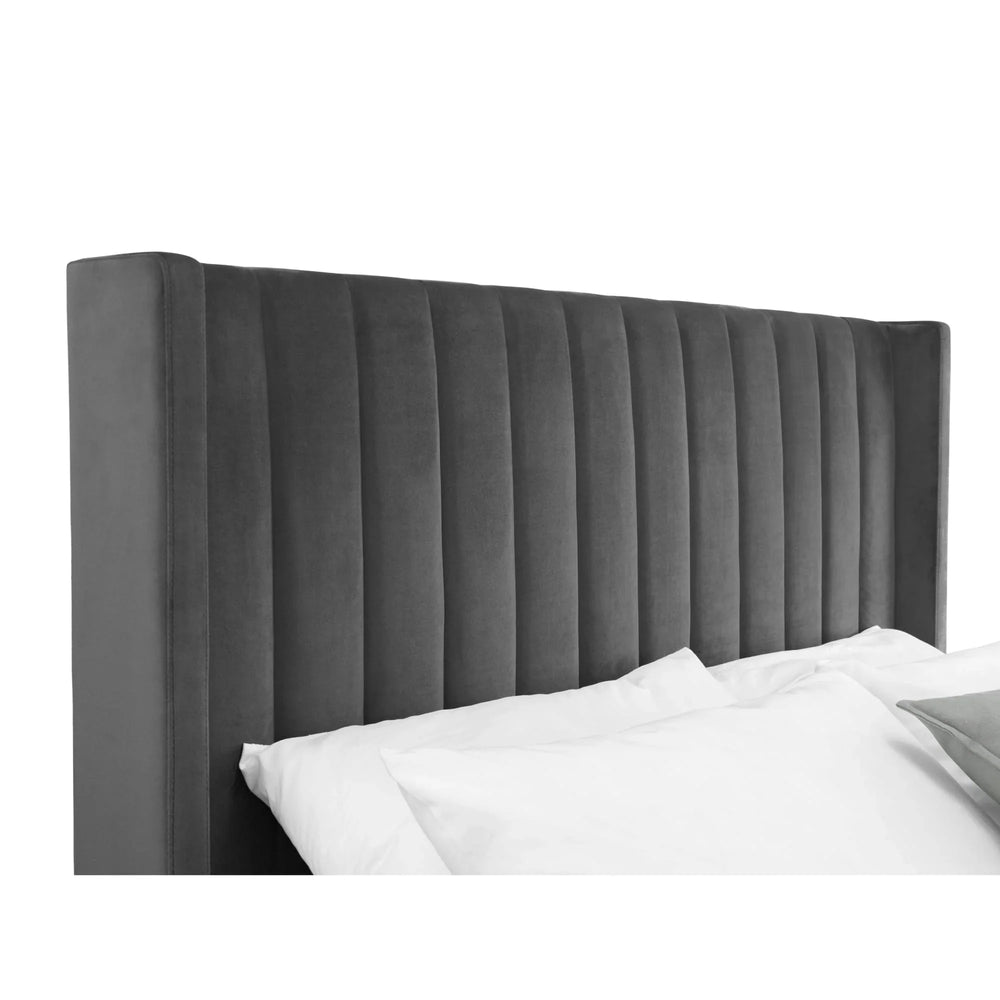 Grey velvet upholstered bed headboard with vertical panel design and pillows