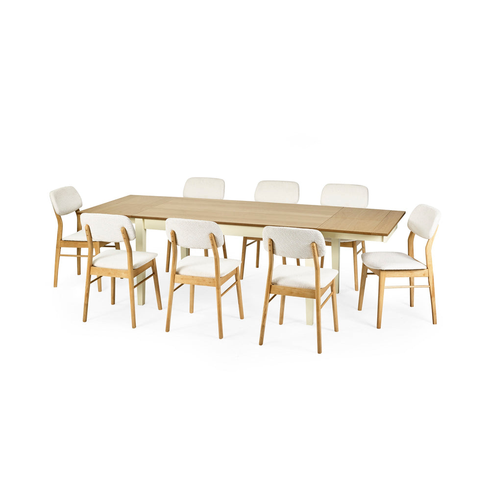 Extended rectangular dining table with cream legs and natural wood top surrounded by eight cushioned wooden chairs.