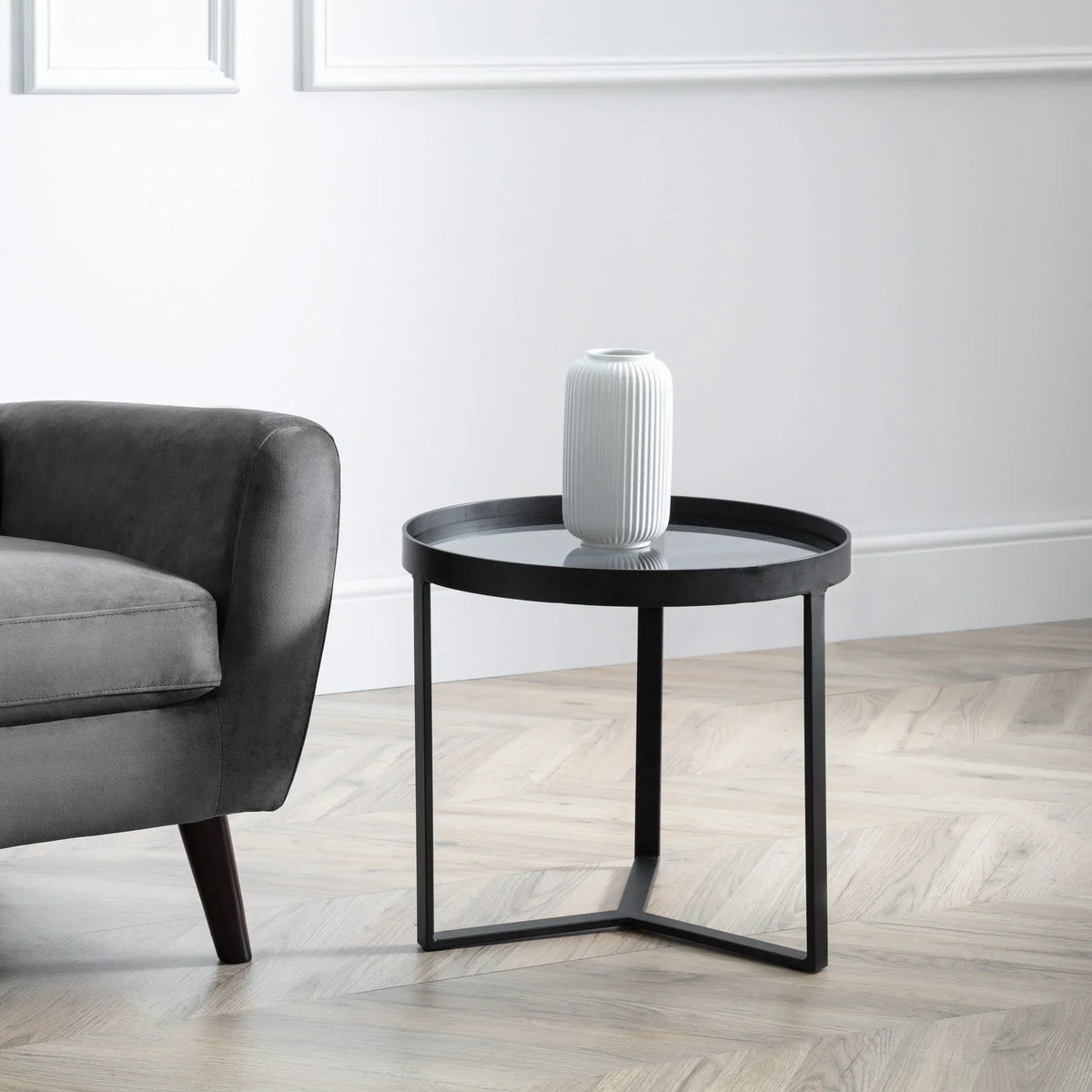 Smoked glass lamp table with black metal frame beside grey upholstered sofa