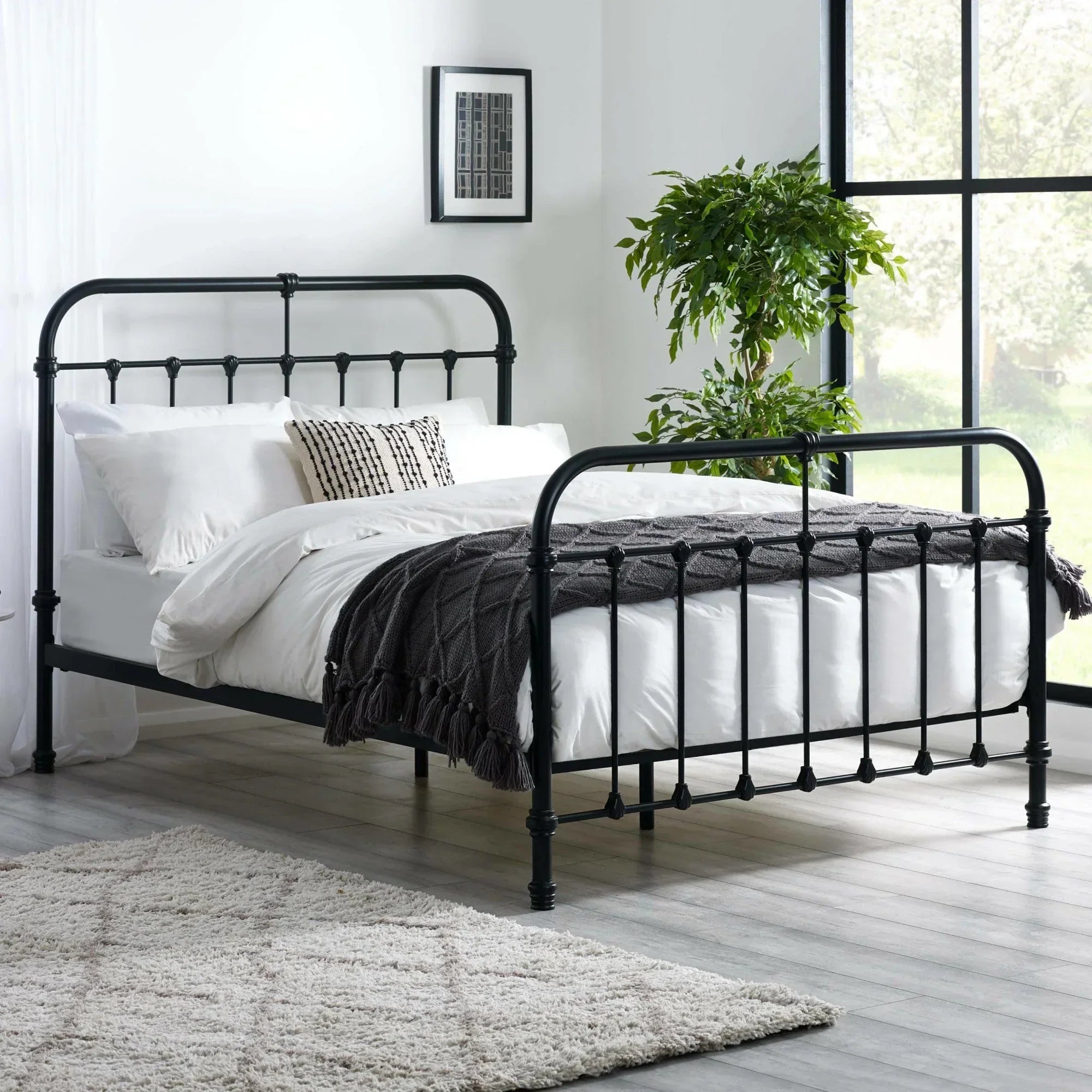 Black metal bed frame with white bedding in modern bedroom with large window and indoor plant
