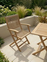 Wooden garden chair and table set on patio with greenery and plants in the background