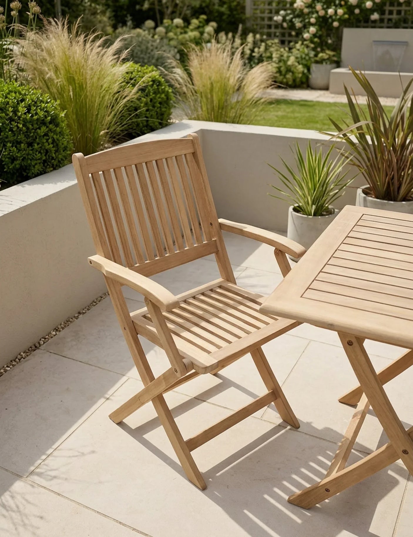 Wooden outdoor garden chair beside slatted patio table on tiled terrace with plants