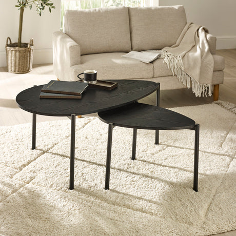 Two black teardrop-shaped nesting coffee tables on fluffy beige carpet in front of beige sofa