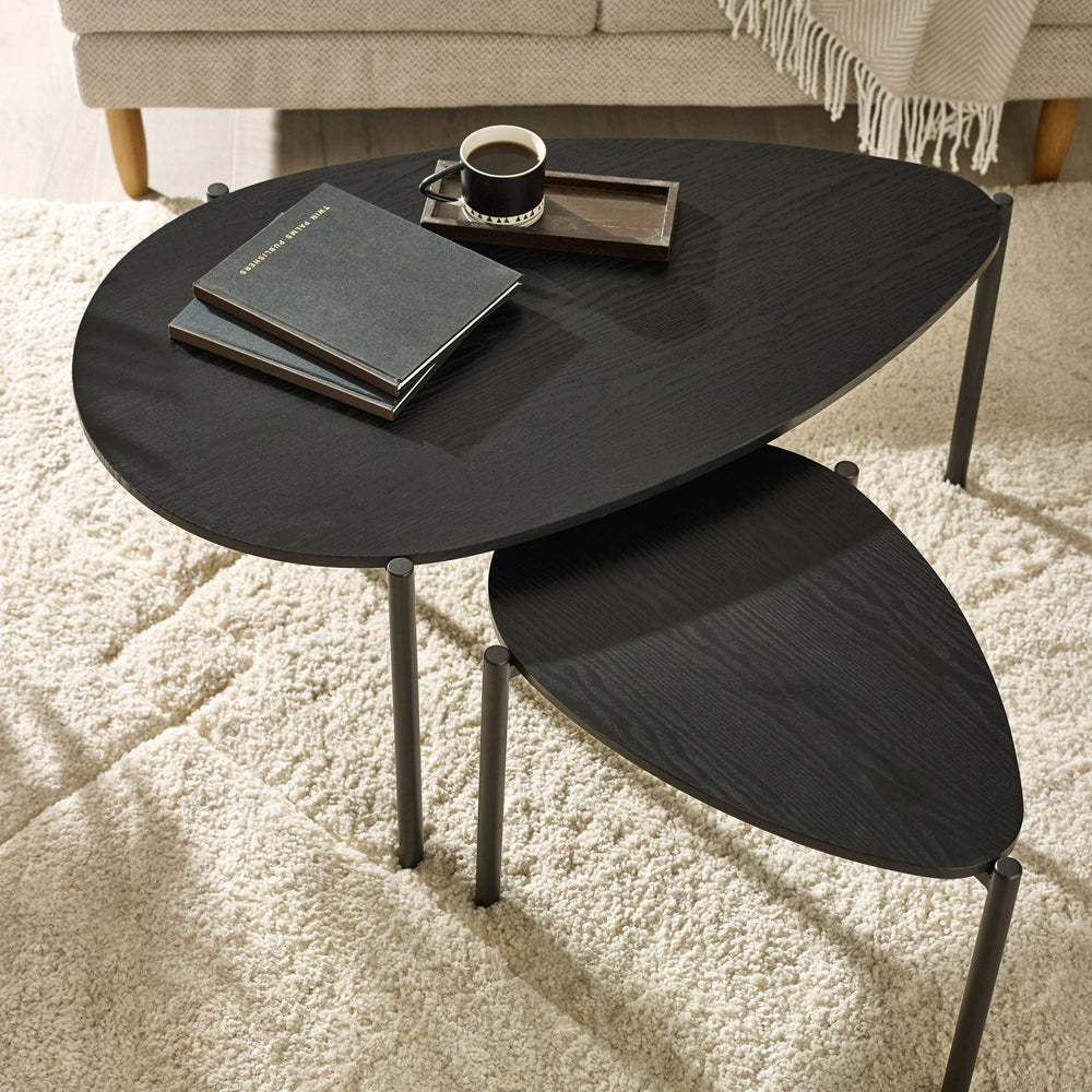 Close-up of black wood teardrop table tops and cylindrical black metal legs on beige carpet