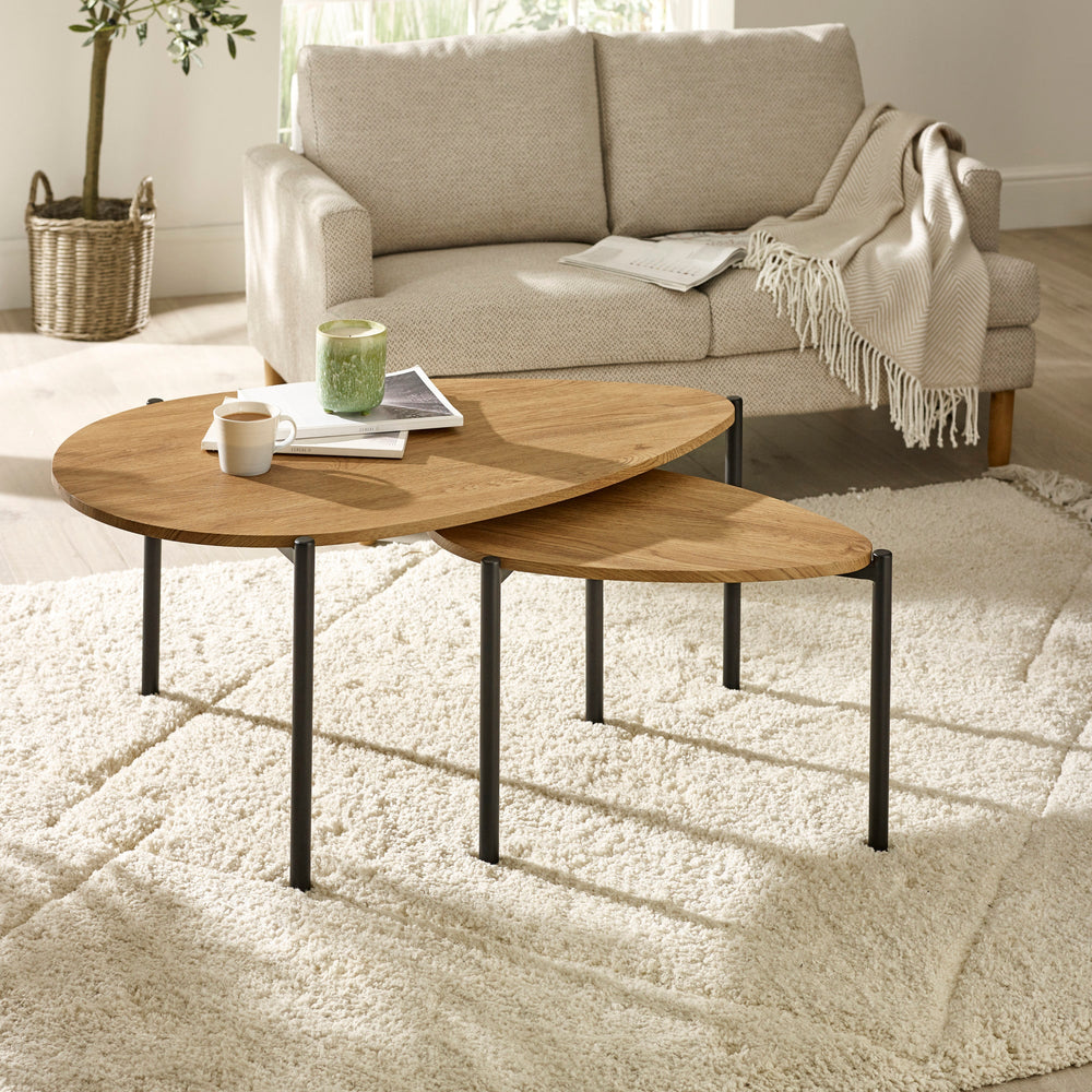 Light oak wood teardrop nesting coffee tables in living room with beige sofa and cream rug.