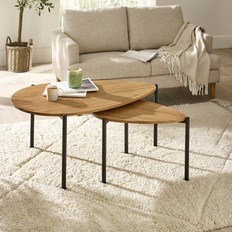 Light oak wood teardrop nesting coffee tables in living room with beige sofa and cream rug.