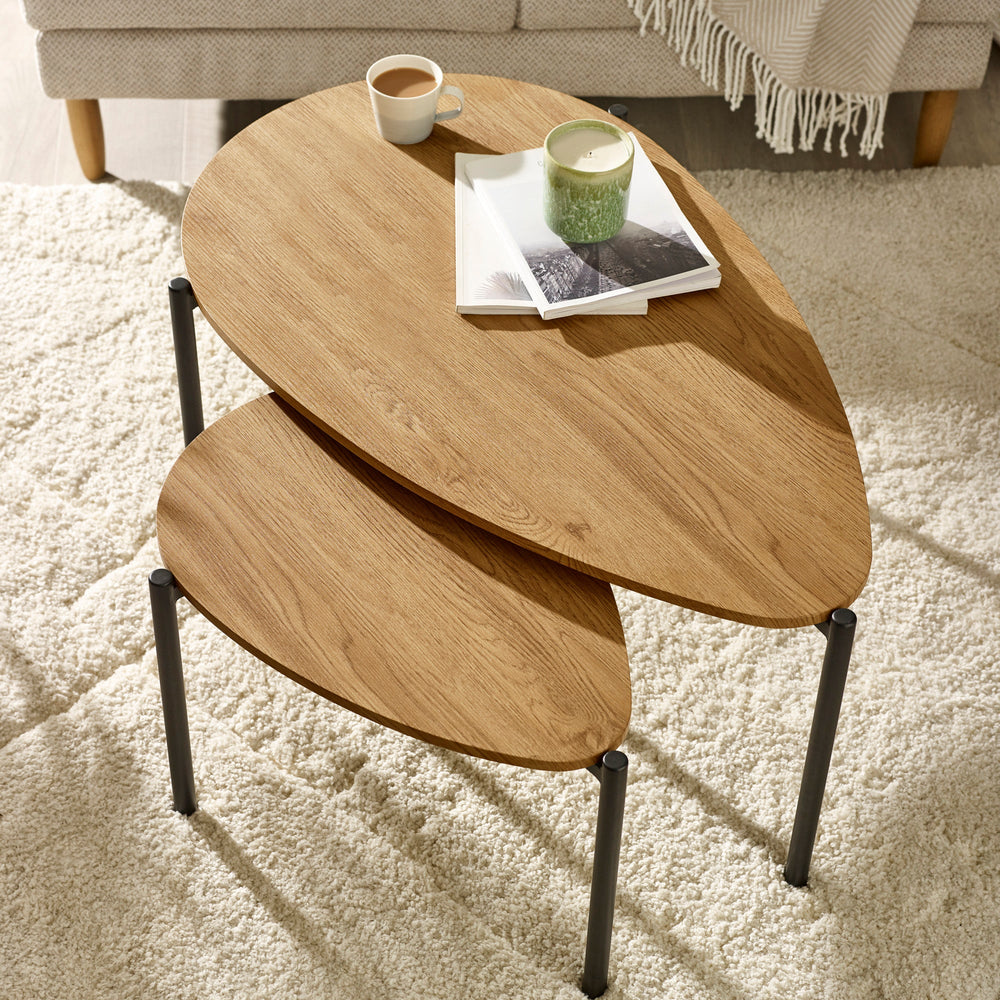 Overhead view of two light oak nesting coffee tables on cream rug with cup, candle, and books.