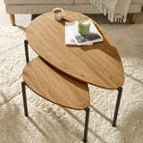 Overhead view of two light oak nesting coffee tables on cream rug with cup, candle, and books.