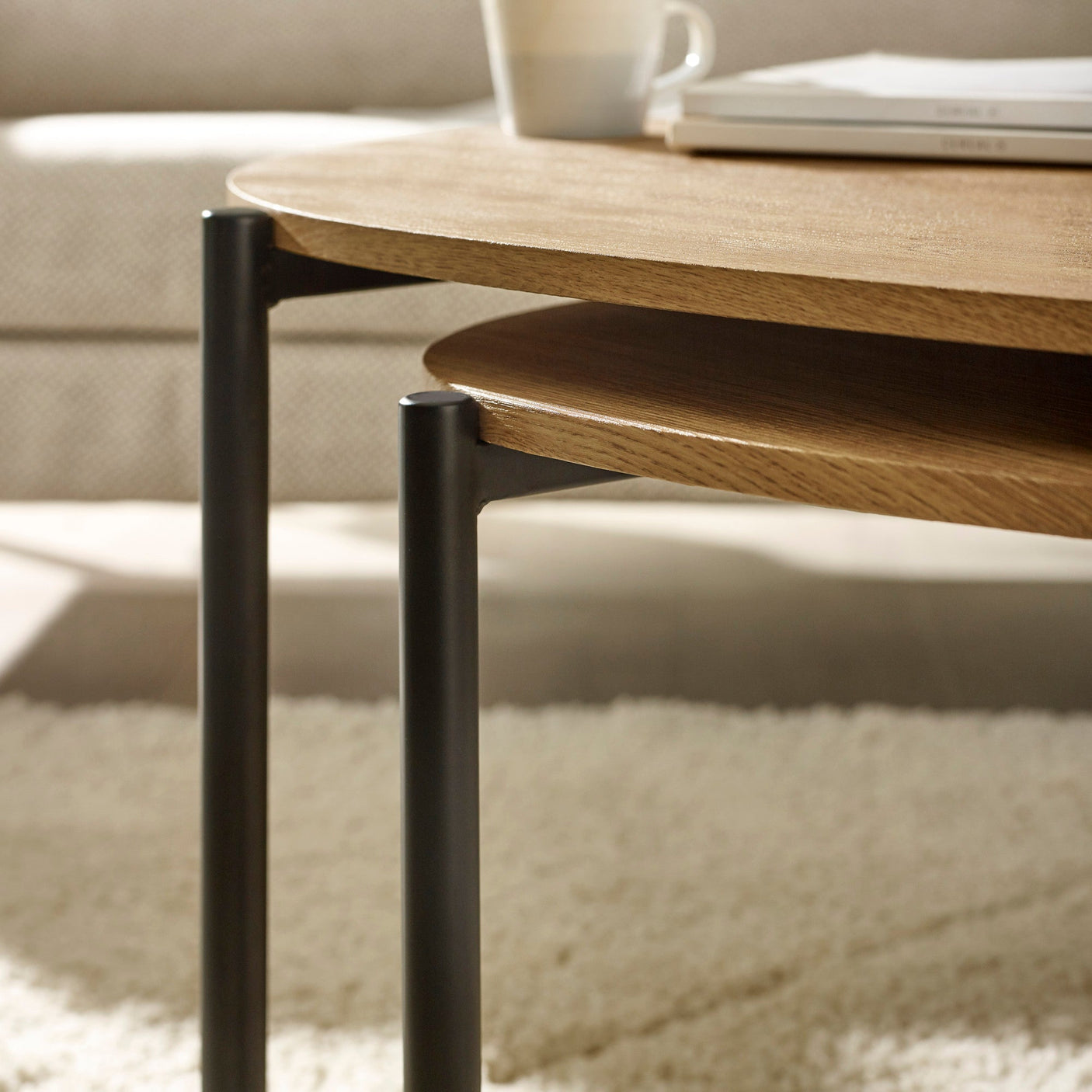 Close-up of light wood teardrop coffee tables with black metal legs, showing layered table tops and details
