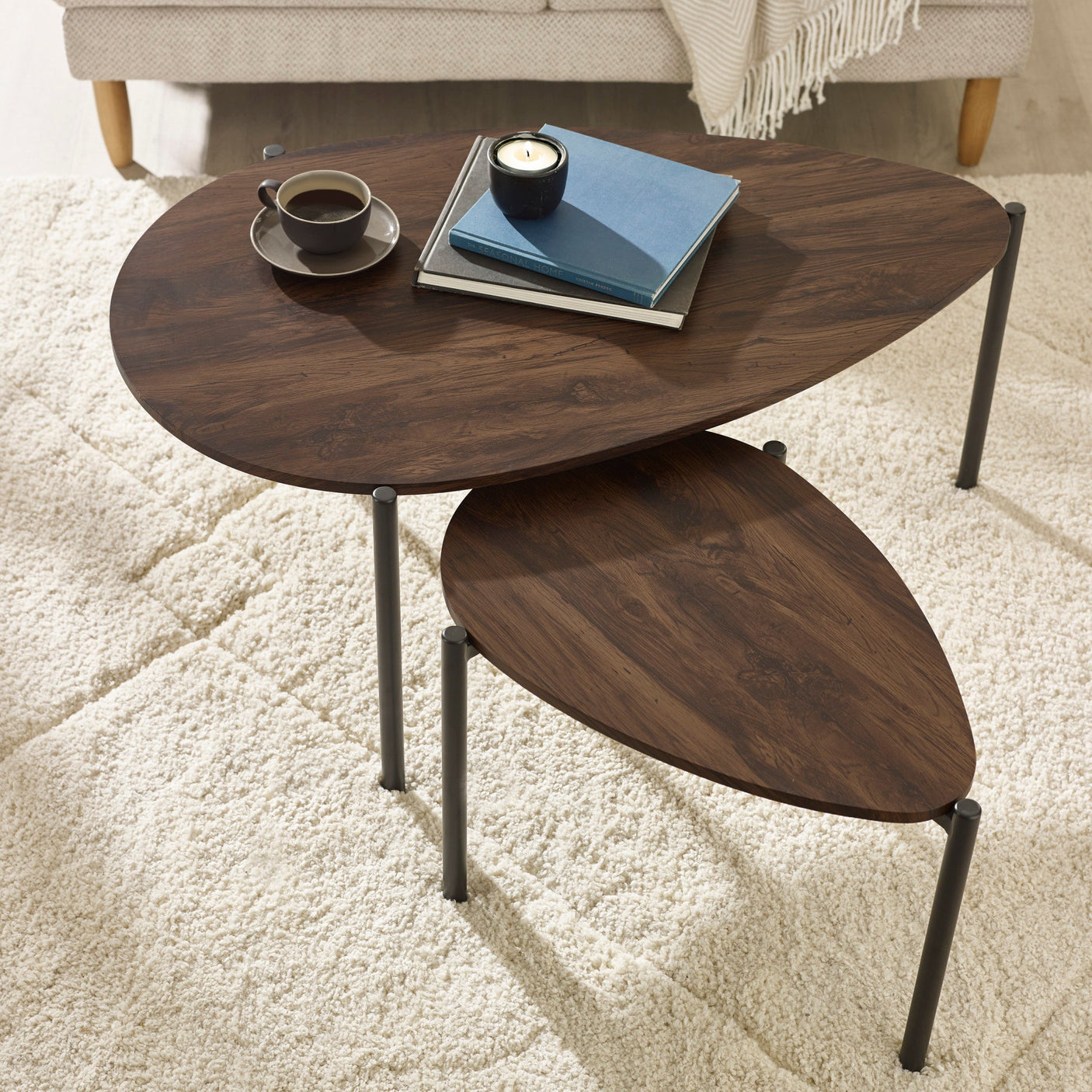 Dark wood teardrop nesting coffee tables with black metal legs in living room, books and cup on top
