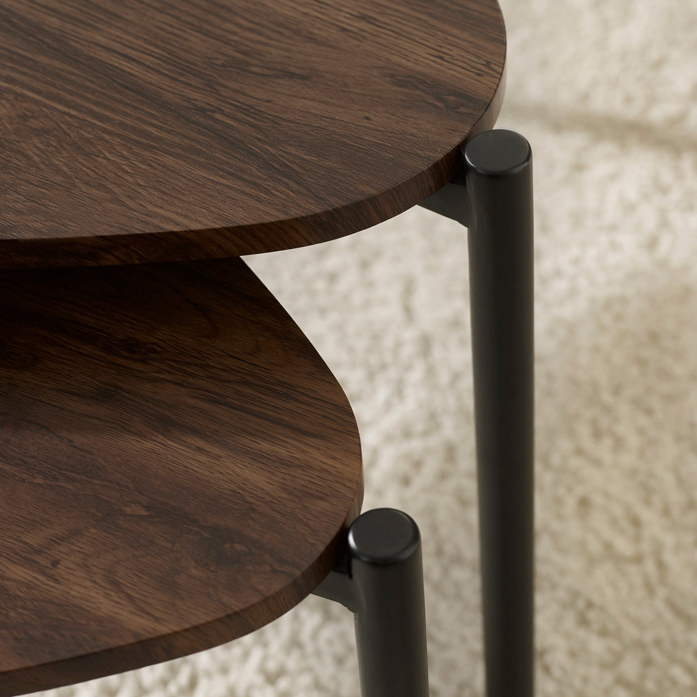 Close-up of dark wood teardrop tabletops with black cylindrical metal legs on cream shag carpet