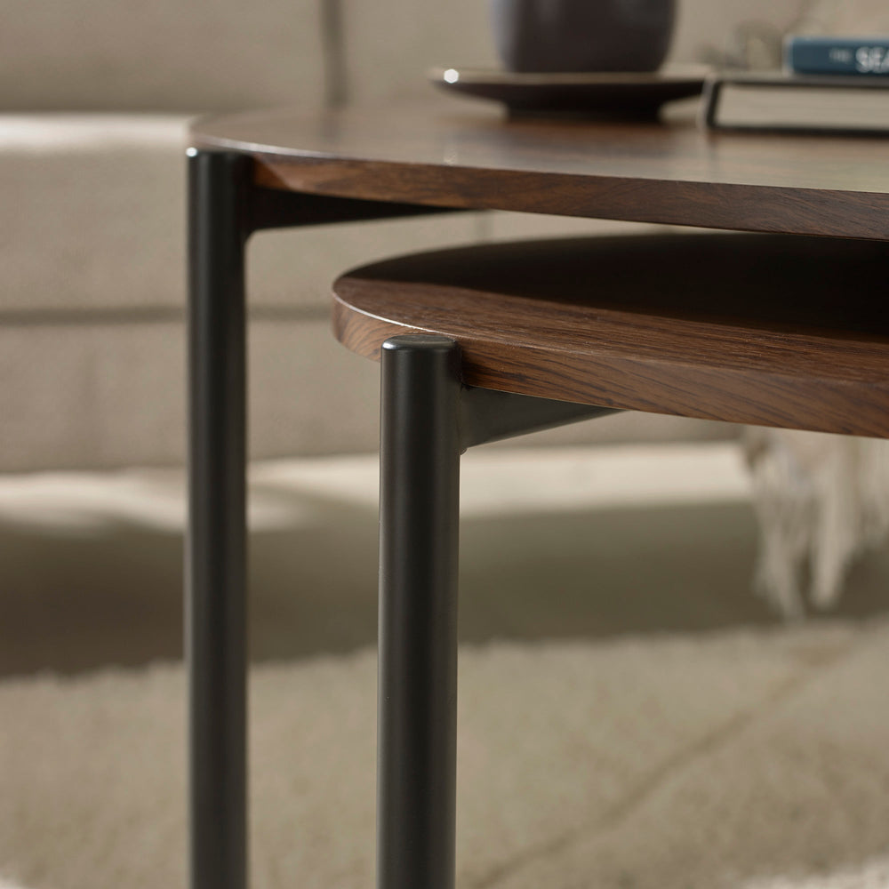 Close-up side view of dark wood teardrop tabletop and black metal legs against light beige sofa background