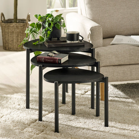 Three black teardrop-shaped nesting side tables with metal legs beside cream armchair on white rug.