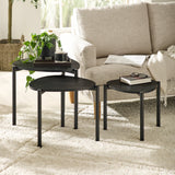 Set of three black teardrop nesting tables with items on top beside textured cream armchair on rug.
