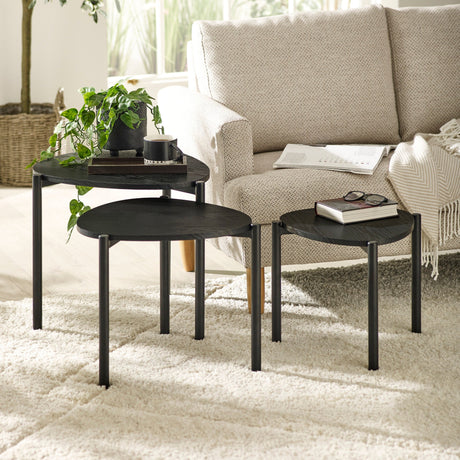 Set of three black teardrop nesting tables with items on top beside textured cream armchair on rug.