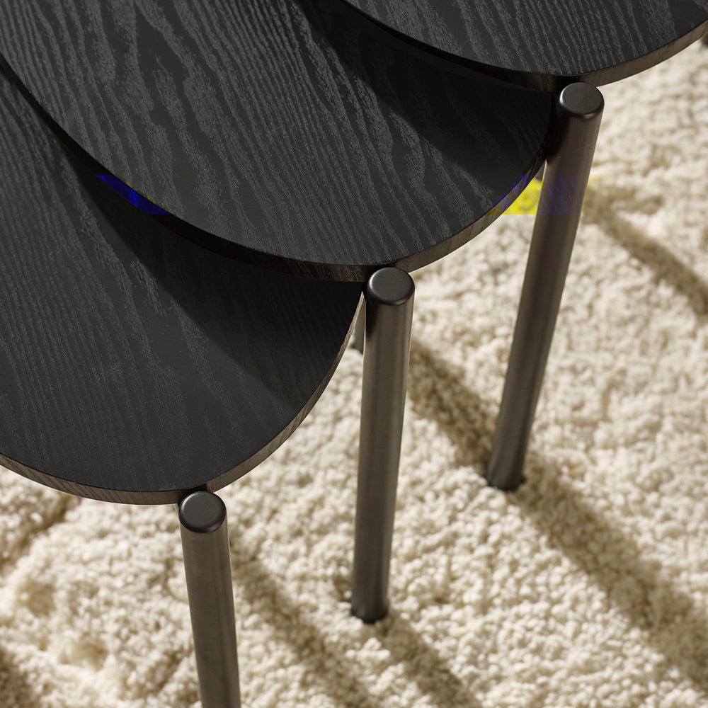 Top angled view of three black teardrop-shaped nesting tables showing shapes, wood grain, and metal legs.