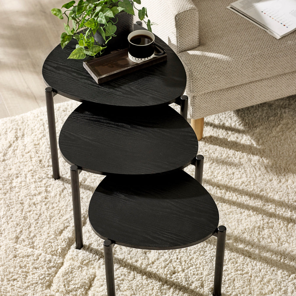 Overhead view of three black teardrop nesting side tables set apart on white textured rug in living room.