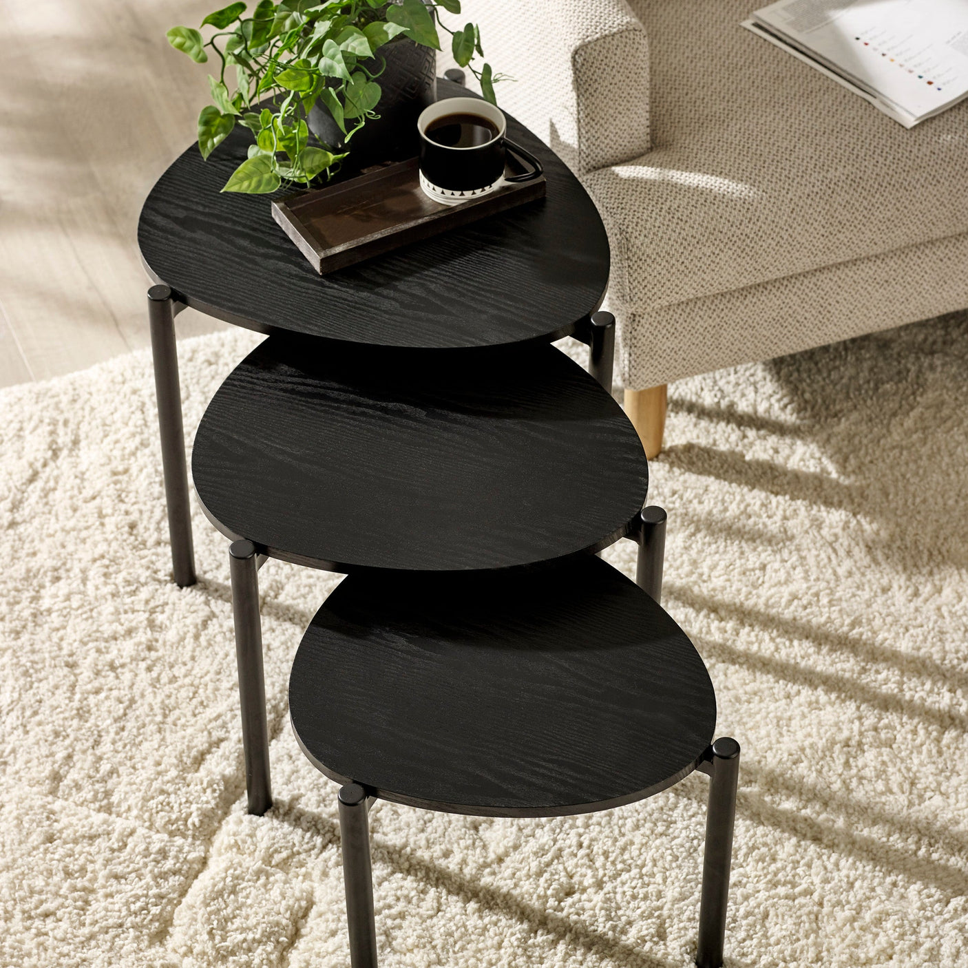 Overhead view of three black teardrop nesting side tables set apart on white textured rug in living room.