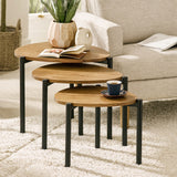 Three nesting side tables with light wood tops and black legs in living room with white armchair.