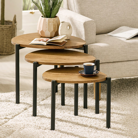Three nesting side tables with light wood tops and black legs in living room with white armchair.