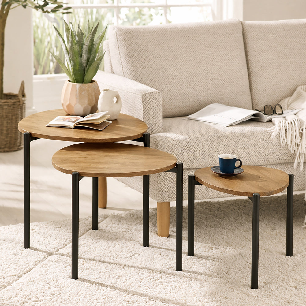 Nesting tables with light wood teardrop tops and black metal legs on cream rug beside sofa.