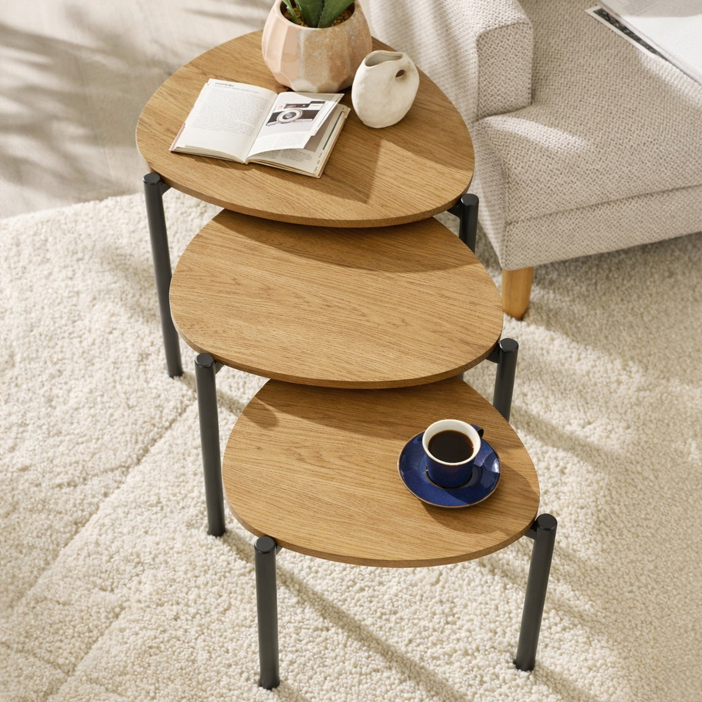 Overhead view of three teardrop nesting tables with light wood tops and black legs on cream carpet.