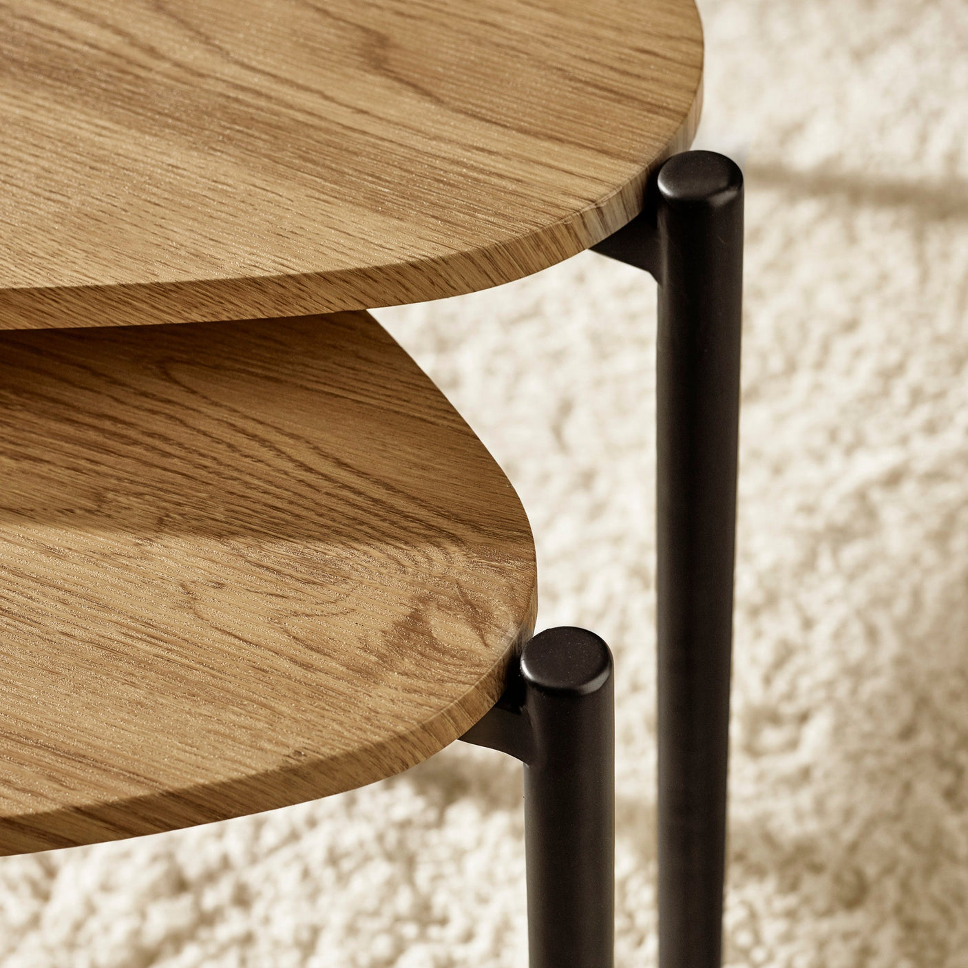 Close-up detail of light wood teardrop tabletops and black metal legs on nesting side tables.