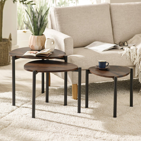 Three dark wood teardrop nesting side tables arranged in front of beige fabric sofa on white rug in living room.