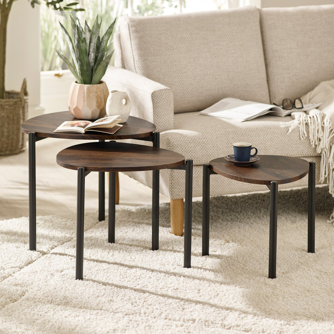 Three dark wood teardrop nesting side tables arranged in front of beige fabric sofa on white rug in living room.