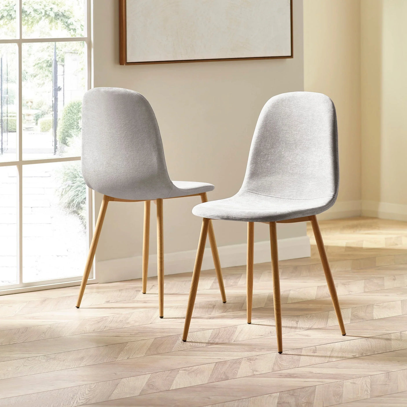 Pair of grey fabric dining chairs with wooden legs on herringbone floor in sunlit room