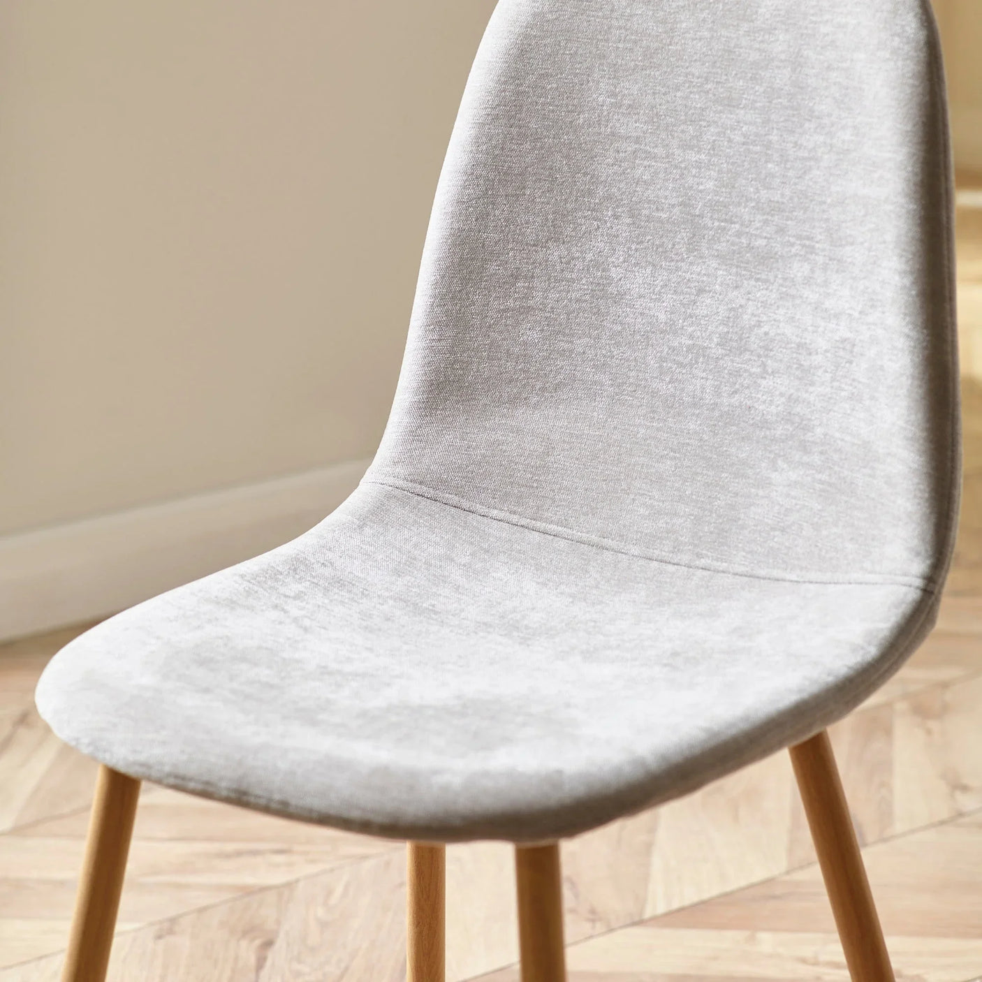 Light grey fabric dining chair with wooden legs on parquet floor, side angle view