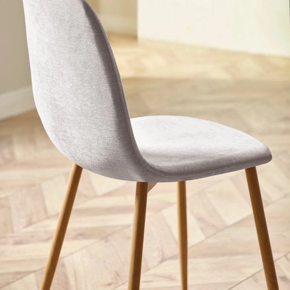 Light grey dining chair with fabric upholstery and wooden legs on herringbone floor