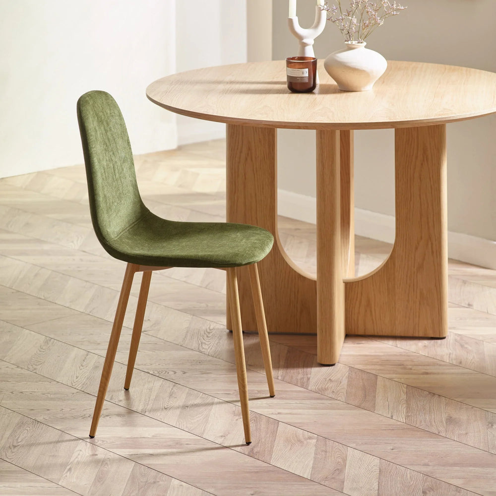 Green velvet dining chair with wooden legs beside round oak dining table