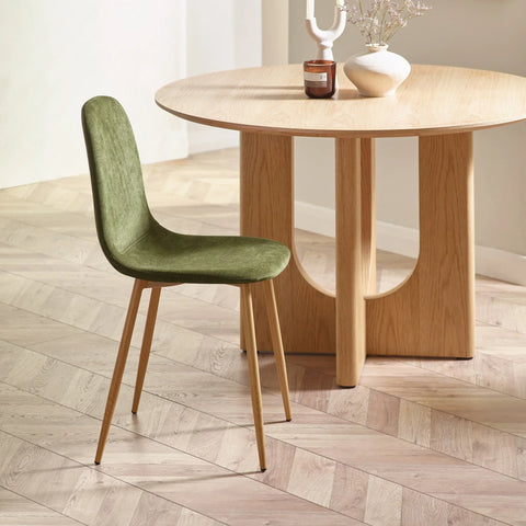 Green velvet dining chair with wooden legs beside round oak dining table