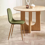 Green velvet dining chair with wooden legs beside round oak dining table