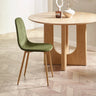 Green velvet dining chair with wooden legs beside round oak dining table