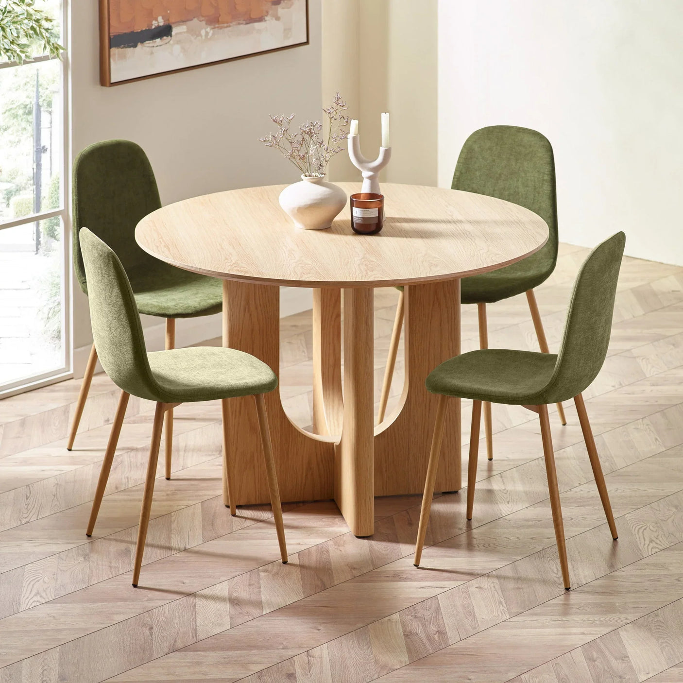 Round oak dining table with sculpted base, four green velvet chairs in modern dining room