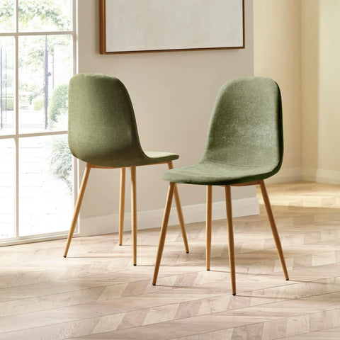 Pair of green velvet dining chairs with wooden legs on herringbone floor in bright room